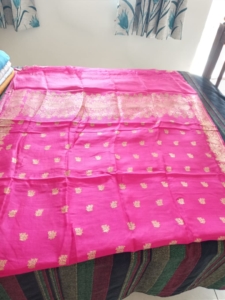 Photo of a shocking pink Banarasi saree with gold brocade aired on a bed.
