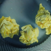 Three crumpled up yellow pieces of paper with some visible but illegible writing, in a waste basket.