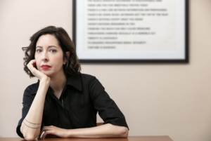 Sarah Manguso in black shirt before poster of words