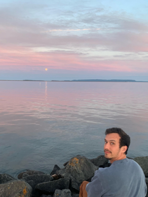 Jonathan Focht sitting on a rock next to the water with a beautiful sky