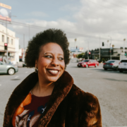 Morgan Parker in brown coat with cars in background