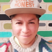 Raquel Gutierrez headshot with painted bricks and white hat