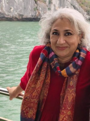 Headshot of Shikhandin smiling at the camera. She is standing in front of a body of water.