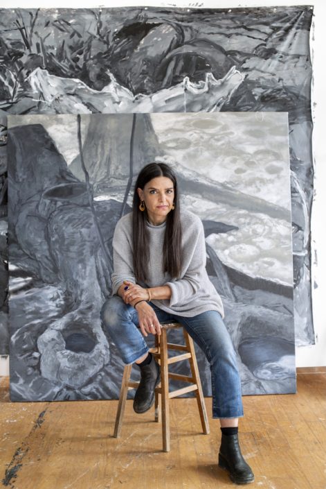 Mariam Aziza Stephan in front of the artwork in a studio seated on a stool looking into the camera.