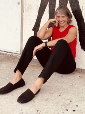 Image of writer Julie Marie Wade sitting on the ground in a red shirt and black pants.