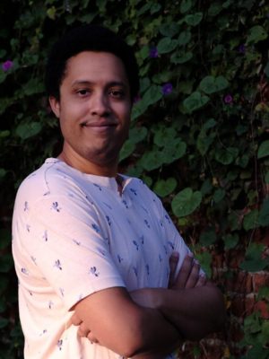 author, smiling, standing outside in front a brick wall covered in morning glory flowers